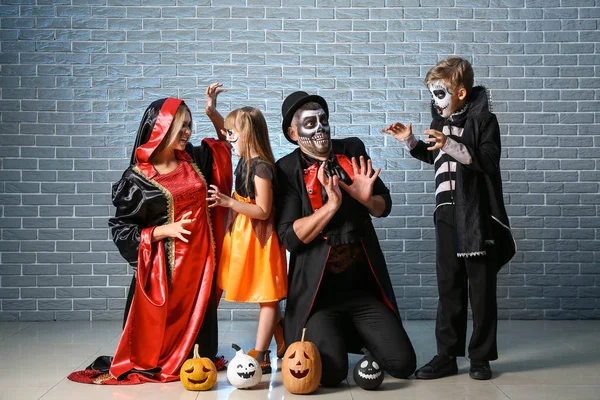 Family in Halloween costumes and with pumpkins on brick background — Stock Photo, Image