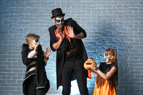 Pai com crianças em trajes de Halloween e com abóbora no fundo de tijolo — Fotografia de Stock