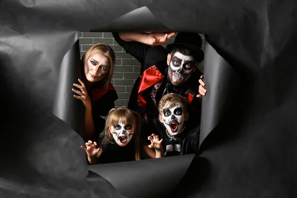 Família em trajes de Halloween olhando para fora do buraco em papel rasgado — Fotografia de Stock