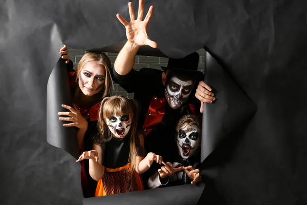 Family in Halloween costumes looking out of hole in torn paper — Stock Photo, Image