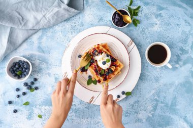 Masada dondurma ve yaban mersinli waffle yiyen bir kadın.