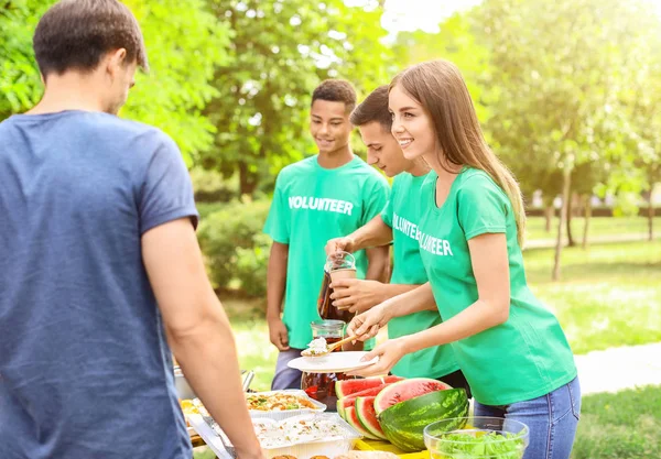 Jovens voluntários dando comida para pessoas pobres ao ar livre — Fotografia de Stock