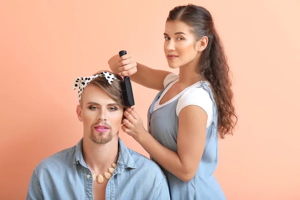 Девушка делает волосы молодой трансгендерной женщины на цветном фоне — стоковое фото