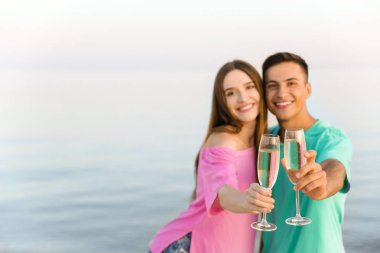 Genç çift deniz sahilinde şampanya içiyor.