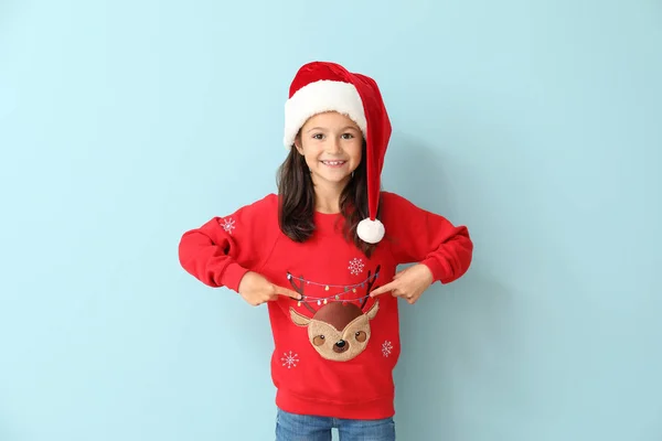 Little girl in Christmas sweater and Santa hat on color background — Stock Photo, Image