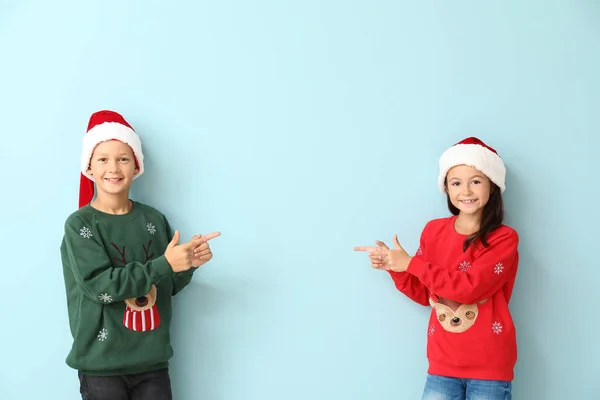 Små barn i jultröjor och Santa hattar pekar på något på färg bakgrund — Stockfoto