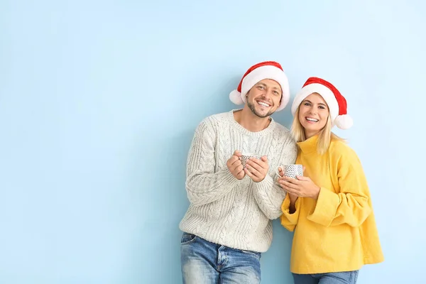 Feliz casal em Santa chapéus beber chocolate quente no fundo de cor — Fotografia de Stock