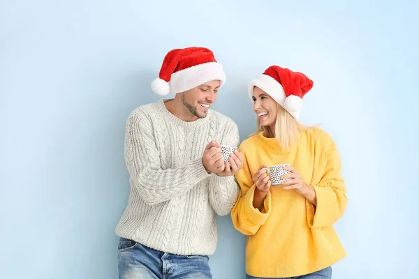 Feliz pareja en los sombreros de Santa beber chocolate caliente en el fondo de color — Foto de Stock