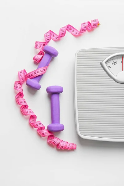 Scales and measuring tape with dumbbells on white background. Weight loss concept — Stock Photo, Image