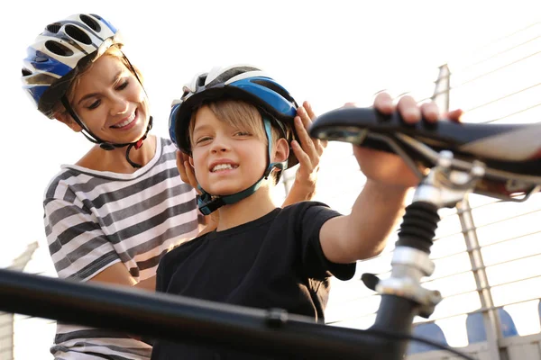 Mãe ajudando seu filho a colocar em capacete de bicicleta ao ar livre — Fotografia de Stock