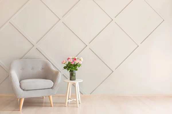 Beautiful rose flowers in vase on table and armchair near grey wall in room — Stock Photo, Image