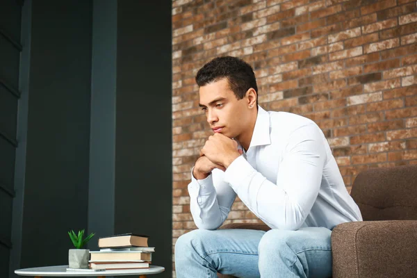 Young African-American man sitting in armchair at home — Stock Photo, Image