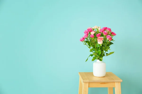 Vase with beautiful rose flowers on stool against color background — Stock Photo, Image