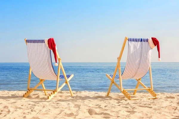 Liegestühle mit Weihnachtsmützen am Strand — Stockfoto