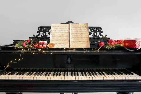 Piano with Christmas decor and sheet music on light background — Stock Photo, Image