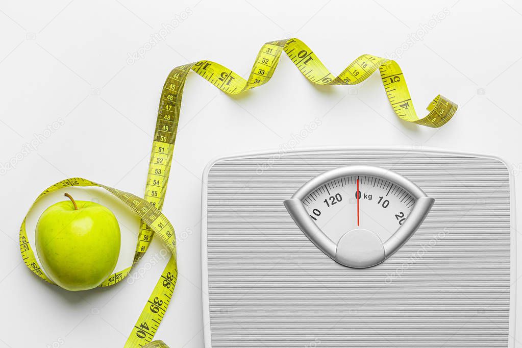 Scales and measuring tape with apple on white background. Weight loss concept