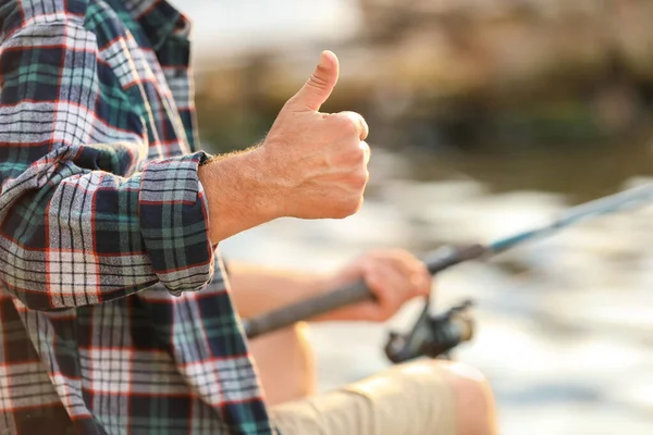 Uomo maturo mostrando pollice in su durante la pesca sul fiume, primo piano — Foto Stock