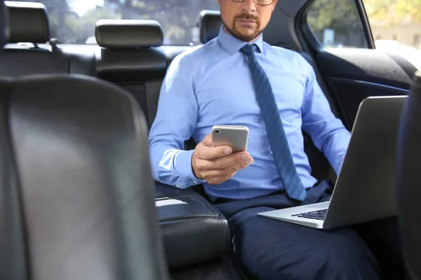Успішний бізнесмен з ноутбуком і мобільним телефоном в сучасному автомобілі — стокове фото