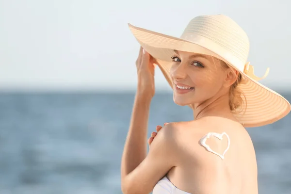 Hermosa joven con corazón dibujado con crema de protección solar en su espalda en el balneario — Foto de Stock