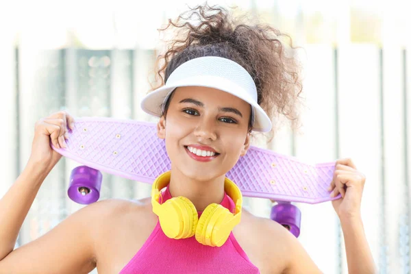 Belle afro-américaine avec écouteurs modernes et planche à roulettes en plein air — Photo