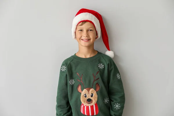 Смешной мальчик в рождественском свитере и шляпе Санты на светлом фоне — стоковое фото