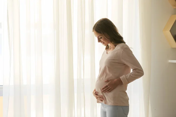 Красивая беременная женщина у окна дома — стоковое фото