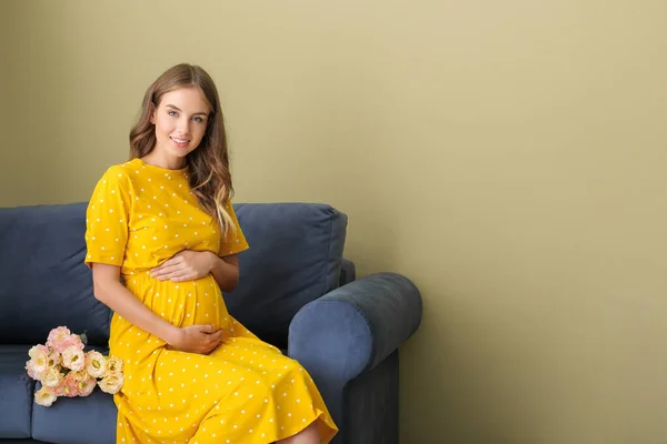 色の背景にソファに座って花の花束を持つ美しい妊娠中の女性 — ストック写真