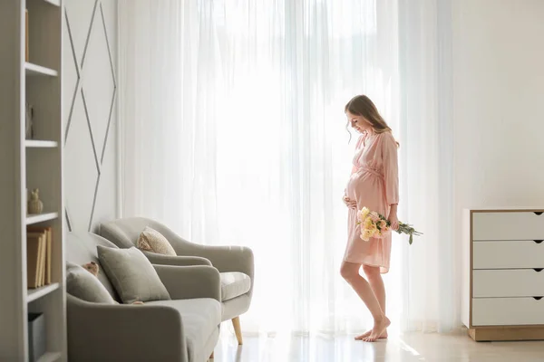 Beautiful pregnant woman with flowers near window — Stock Photo, Image