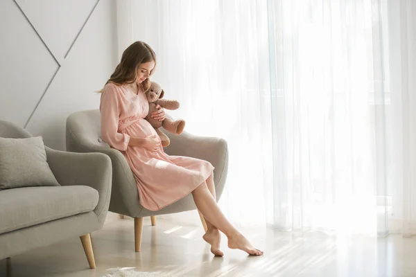 Mulher grávida bonita com brinquedo sentado em poltrona em casa — Fotografia de Stock