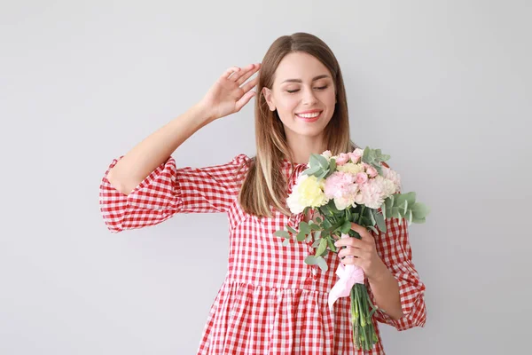 Beautiful young woman with bouquet of carnation flowers on light background — Stock Photo, Image