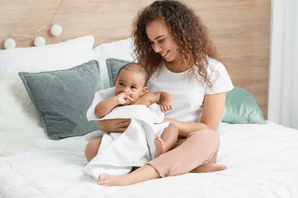 Young African-American mother with cute baby sitting on bed after bathing — Stock Photo, Image