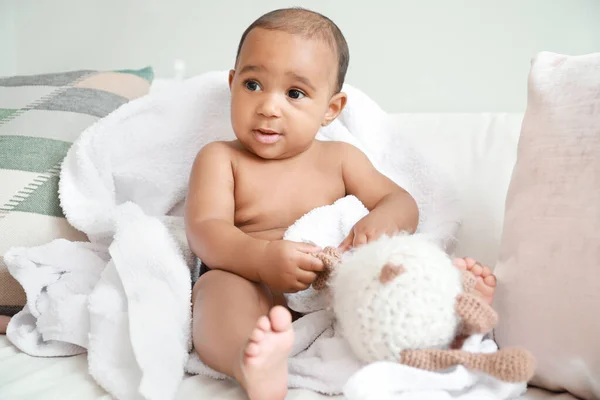 Süßes afrikanisch-amerikanisches Baby mit weichem Handtuch und Spielzeug auf dem Bett zu Hause — Stockfoto
