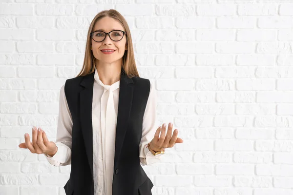 Businesswoman inviting viewer against white brick wall — Stock Photo, Image