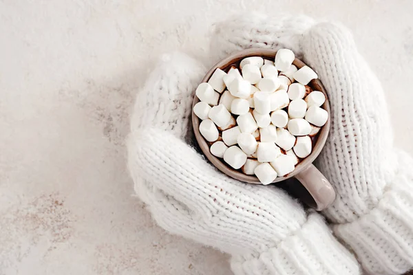 Női kéz kesztyűben, forró csokoládéval és mályvacukorral könnyű háttéren — Stock Fotó