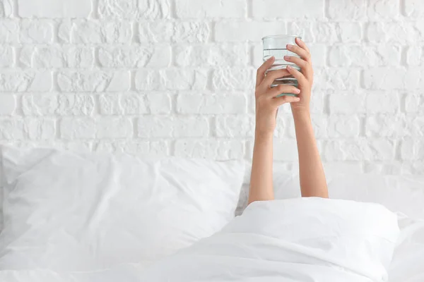 Young woman with glass of water lying in bed — Stock Photo, Image