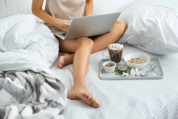 Young woman using laptop while having breakfast in bed — Stock Photo, Image