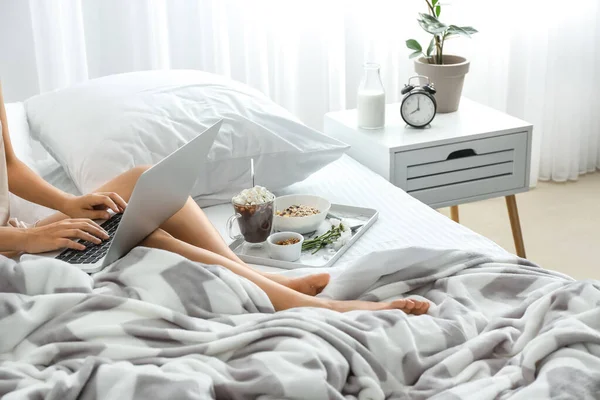 Young woman using laptop while having breakfast in bed — Stock Photo, Image