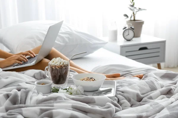 Young woman using laptop while having breakfast in bed — Stock Photo, Image