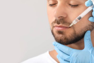 Gri arkaplanda doldurucu enjeksiyon alan yakışıklı adam, yakın plan.