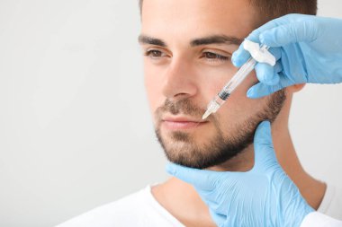 Yakışıklı adam gri arka plan üzerinde dolgu enjeksiyonu alan