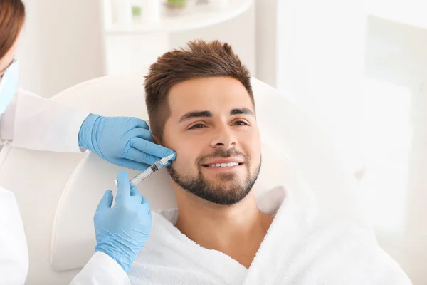 Handsome man receiving filler injection in beauty salon