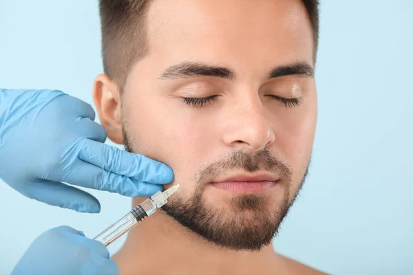 Schöner Mann erhält Füllstoffspritze auf farbigem Hintergrund — Stockfoto