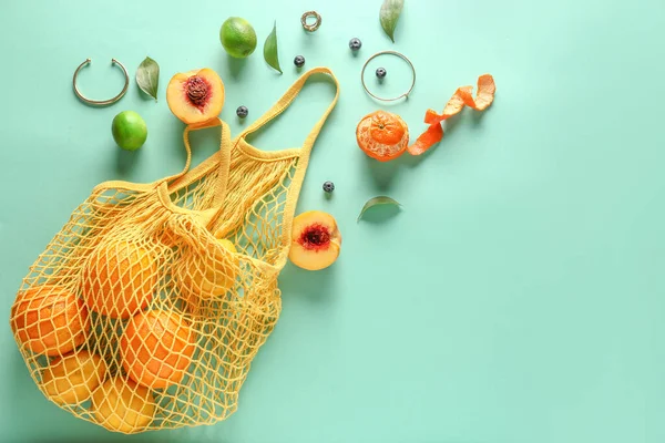 Mesh bag with fresh fruits on color background