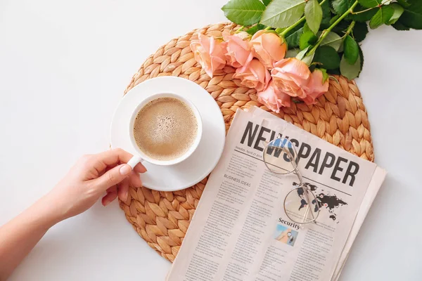 Жіноча рука з чашкою кави, трояндовими квітами та газетою на білому тлі — стокове фото