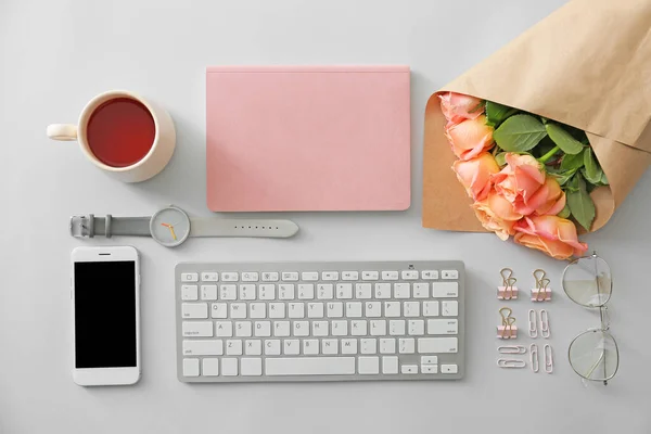 Rose flowers with computer keyboard, mobile phone, cup of tea, stationery and female accessories on white background