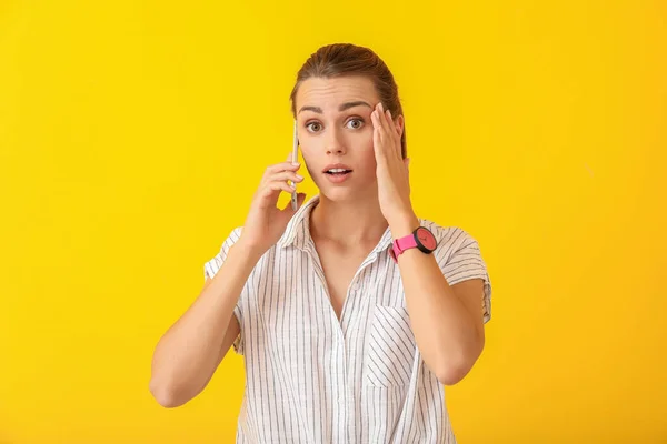 Worried young woman talking by phone on color background — Stock Photo, Image