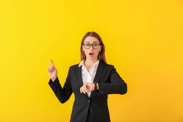 Worried young businesswoman with watch pointing at something on color background — Stock Photo, Image