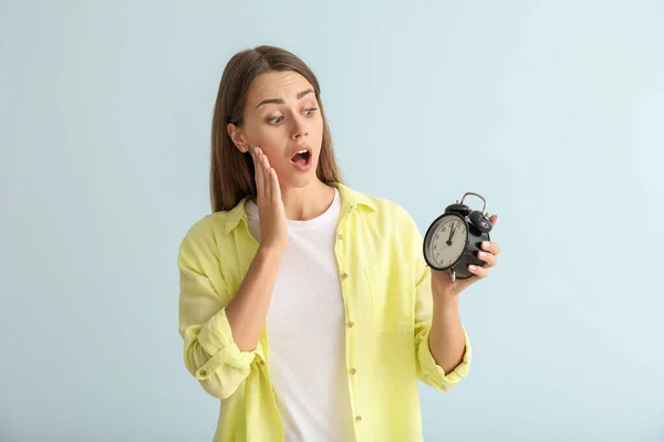 Worried young woman with alarm clock on color background — Stock Photo, Image
