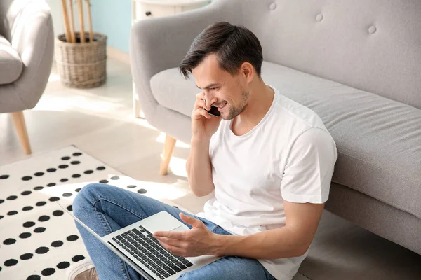 Hombre guapo con portátil hablando por teléfono en casa — Foto de Stock