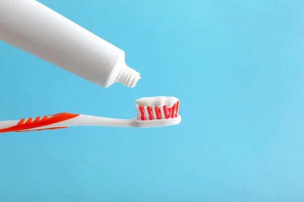 Squeezing of tooth paste from tube onto brush against color background